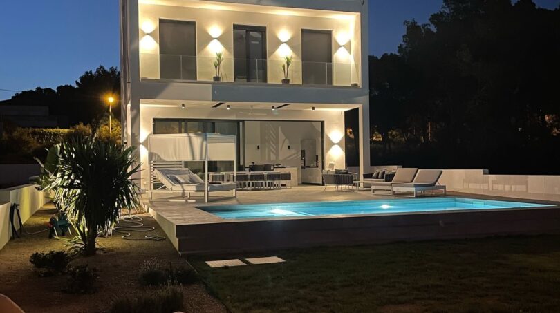 Moderne Villa in Cala Pi bei Nacht mit beleuchtetem Pool, Loungebereich und zweistöckiger weißer Fassade