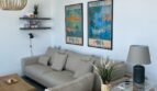 Helles Wohnzimmer mit grauem Sofa, Holzcouchtisch und Mallorca-Vintage-Postern an weißer Wand.