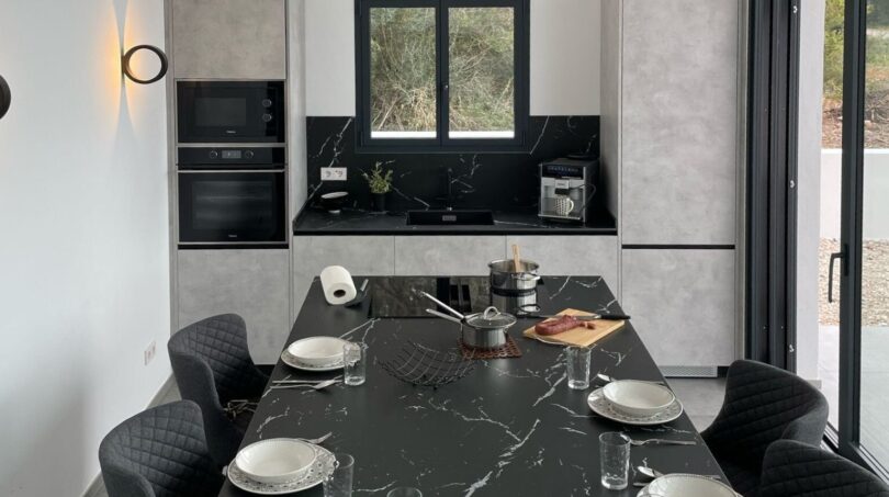 Modernes Esszimmer mit schwarzem Marmortisch, grauen Designerstühlen und offener Küche in Cala Pi