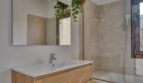 Modernes Badezimmer mit Holzwaschtisch, Wandspiegel, Badewanne mit Dusche und Hängepflanze im Stadthaus Alaró