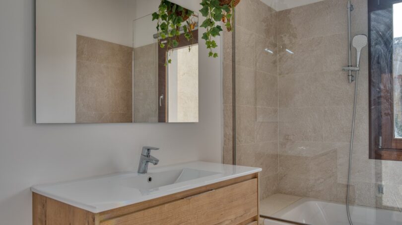 Modernes Badezimmer mit Holzwaschtisch, Wandspiegel, Badewanne mit Dusche und Hängepflanze im Stadthaus Alaró
