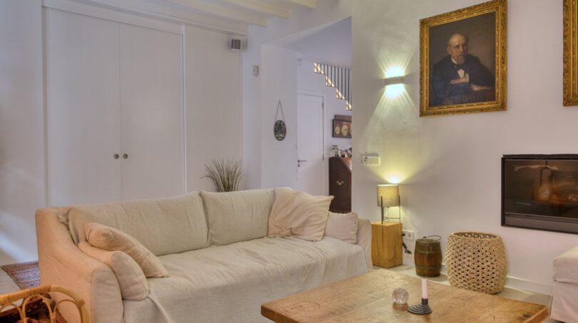 Helles Wohnzimmer mit Leinensofa, Holztisch, Fliesenböden und historischem Gemälde im Stadthaus Alaró