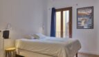 Helles Schlafzimmer mit Doppelbett, Holzbalken, Balkon und blauem Vorhang im Stadthaus Alaró