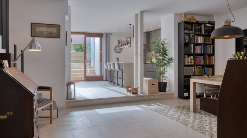 Offener Wohnbereich mit Fliesenboden, Bücherregal und Blick zur Glasfront im Stadthaus Alaró