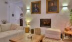 Wohnzimmer des Stadthauses in Alaró mit Sofa, Holztisch, Kamin und historischen Porträts an der Wand.