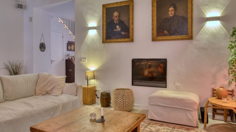 Wohnzimmer des Stadthauses in Alaró mit Sofa, Holztisch, Kamin und historischen Porträts an der Wand.