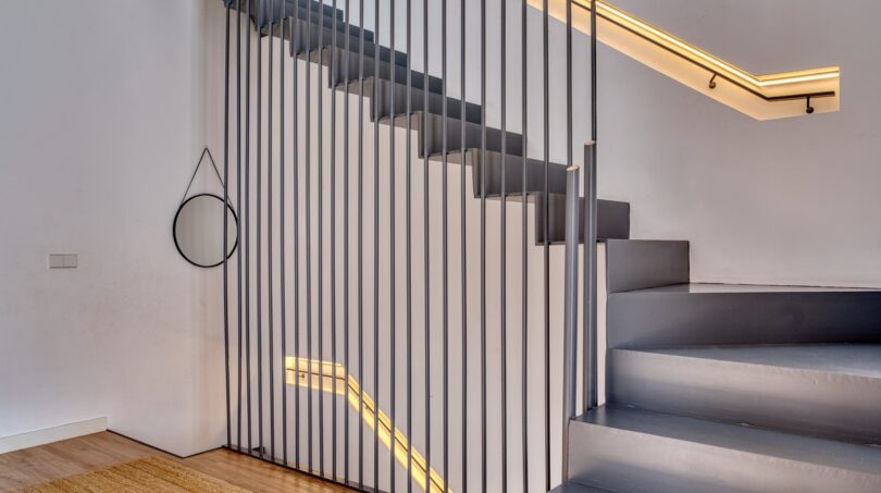 Modernes Treppenhaus mit grauer Betontreppe, schwarzem Metallgeländer und warmem LED-Licht im Stadthaus Alaró