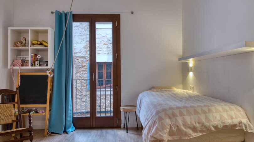Helles Schlafzimmer mit Einzelbett, Balkon und türkisfarbenem Vorhang im modernisierten Stadthaus in Alaró.