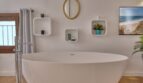 Modernes Badezimmer mit freistehender Badewanne, Wandregalen und goldenem Spiegel im Stadthaus Alaró