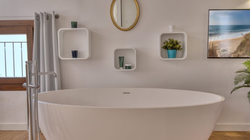 Modernes Badezimmer mit freistehender Badewanne, Wandregalen und goldenem Spiegel im Stadthaus Alaró