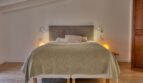 Helles Schlafzimmer mit Doppelbett, grauem Polsterkopfteil und warmem Ambiente im Stadthaus Alaró.