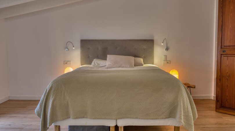 Helles Schlafzimmer mit Doppelbett, grauem Polsterkopfteil und warmem Ambiente im Stadthaus Alaró.