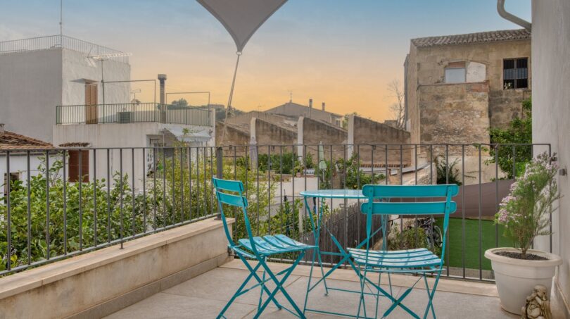 Dachterrasse mit türkisfarbenem Bistro-Set und Sonnensegel, Blick über die Dächer von Alaró bei Sonnenuntergang