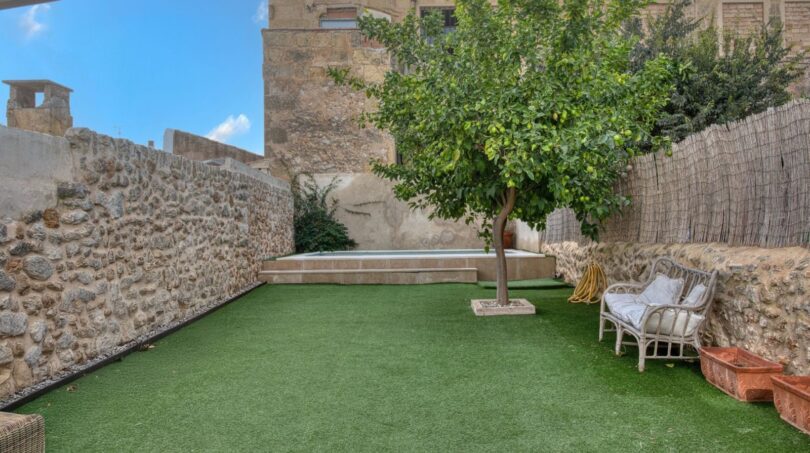 Gepflegter Innengarten mit Kunstrasen, Zitronenbaum, Pool und Natursteinmauern des Stadthauses in Alaró