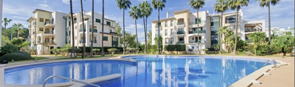 Communal pool with blue water, palm trees and Mediterranean apartment buildings in Santa Ponça
