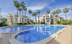 Piscina comunitaria con agua azul, palmeras y edificios de viviendas multifamiliares mediterráneos en Santa Ponça