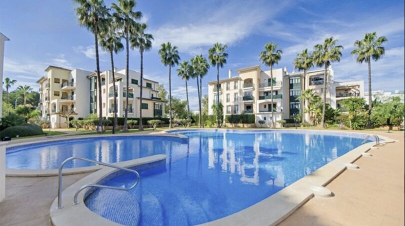 Communal pool with blue water, palm trees and Mediterranean apartment buildings in Santa Ponça