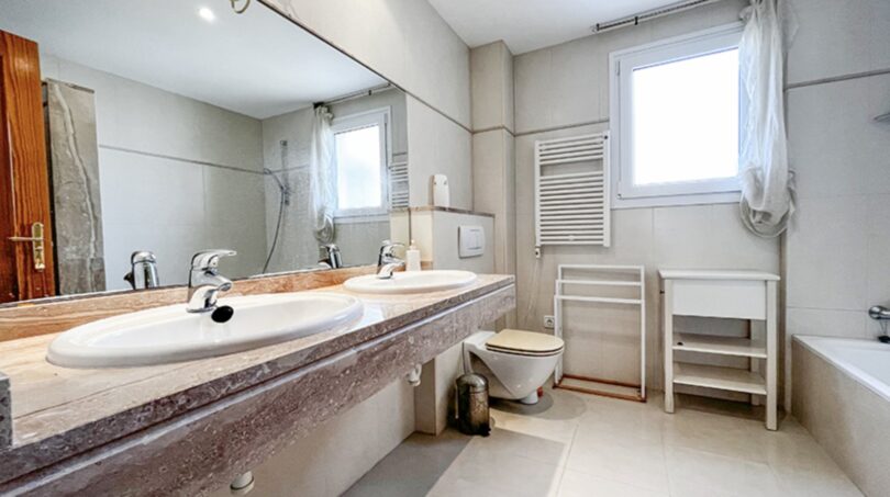 Bright bathroom with double washbasin on marble top, bathtub, toilet and two windows in Villa Santa Ponça