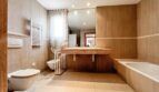 Spacious bathroom with marble washbasin, bathtub, bidet and heater in warm beige tones.