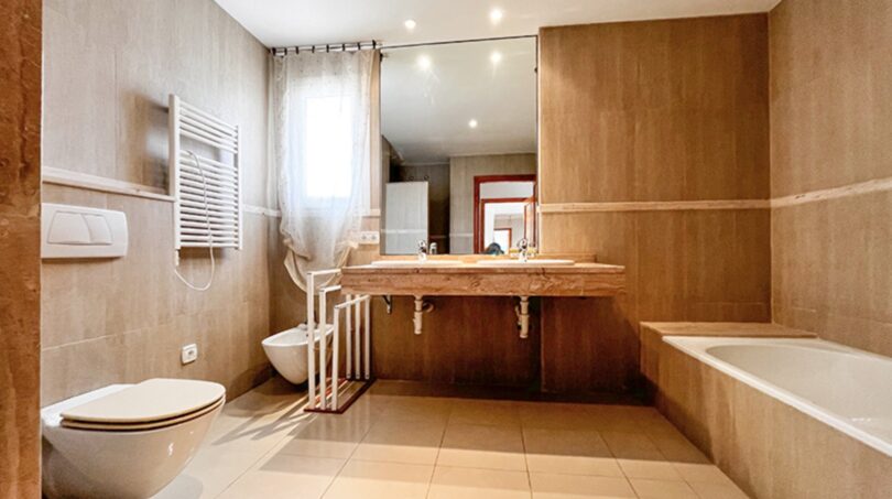 Spacious bathroom with marble washbasin, bathtub, bidet and heater in warm beige tones.