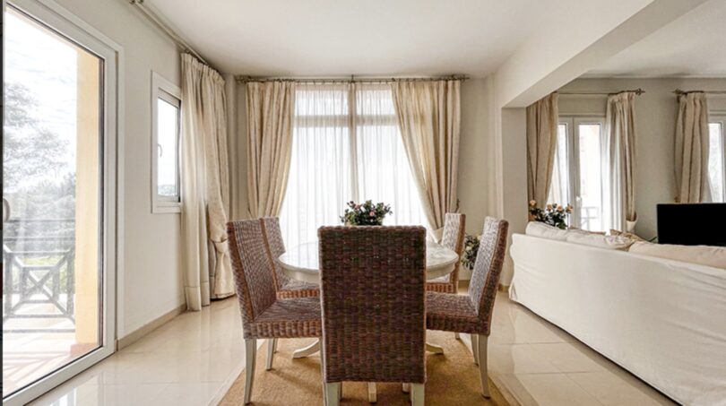 Bright dining area with rattan chairs, round table, terrace access and elegant curtains in Santa Ponça