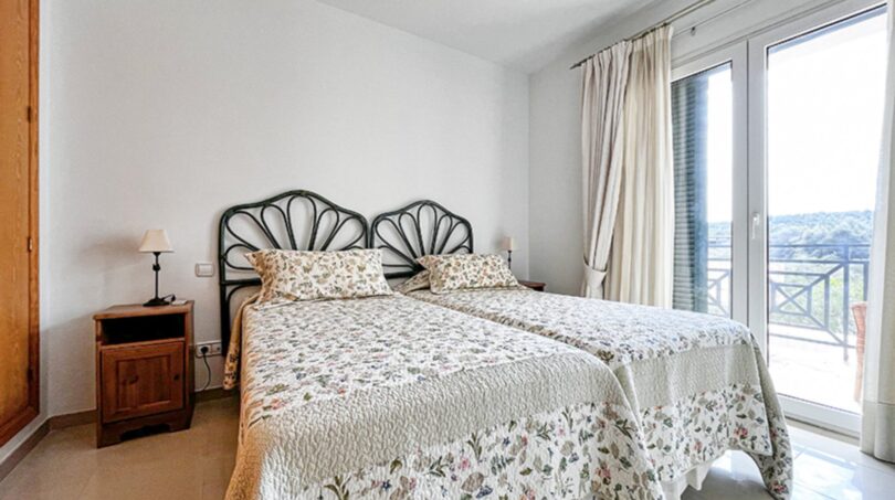 Bright bedroom with two single beds, floral bedding and balcony access with sea views in Santa Ponça