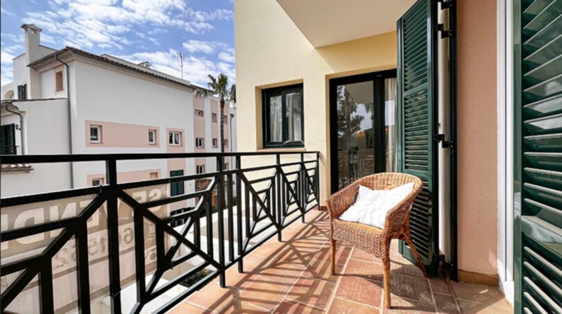 Sunny balcony with rattan chair, green shutters and view of Mediterranean neighboring buildings in Santa Ponça.
