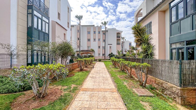 Well-maintained garden path between modern residential buildings in Santa Ponça with Mediterranean palm trees and ornamental shrubs.