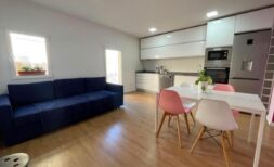 Open living-dining area with blue sofa, white dining table, pink chairs and modern fitted kitchen in Inca.