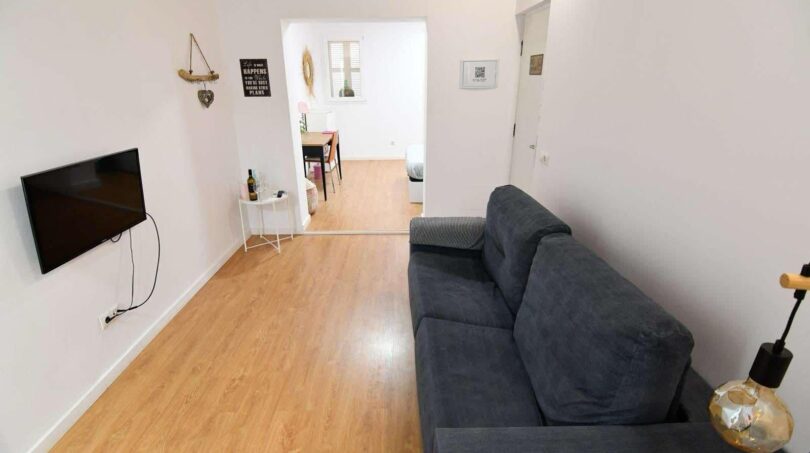 Helles Wohnzimmer mit grauem Sofa, Flachbild-TV und Laminatboden in moderner Wohnung in Inca.