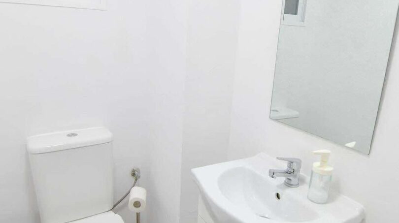 Modernes weißes Badezimmer mit WC, Waschtisch, Spiegel und blauem Handtuch in Inca