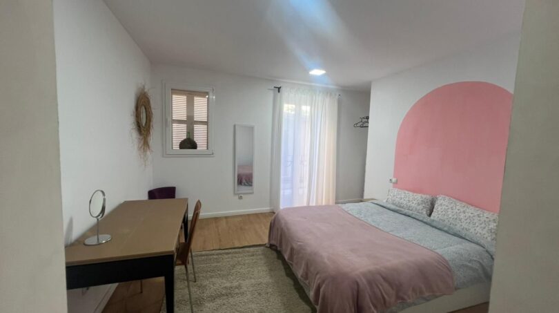 Helles Schlafzimmer mit rosa Akzentwand, Doppelbett, Schreibtisch und Parkettboden in Inca