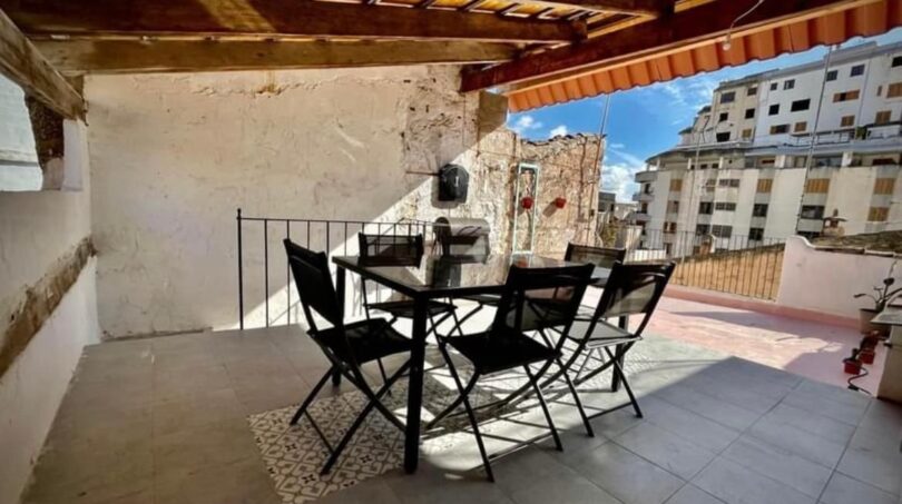 Überdachte Dachterrasse mit schwarzen Gartenmöbeln, Holzbalken und Stadtblick in Inca.