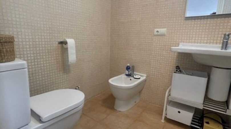 Helles Badezimmer mit WC, Bidet und Waschtisch, cremefarbenen Mosaikfliesen und moderner Beleuchtung im Penthouse Palma.