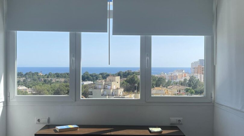 Helles Schlafzimmer im Penthouse mit Doppelbett, Holzkopfteil und Panoramafenster mit Meerblick über Palma de Mallorca.