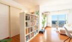 Helles Penthouse-Wohnzimmer mit Regalraumteiler, Holzboden und großer Glasfront mit Meerblick in Palma