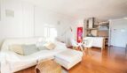 Helles Wohnzimmer mit weißem Sofa, Holzboden und offener Küche im Penthouse Palma de Mallorca