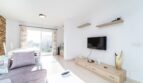 Helles Wohnzimmer in Artà mit grauem Sofa, Holz-TV-Möbel und Zugang zur sonnigen Terrasse.
