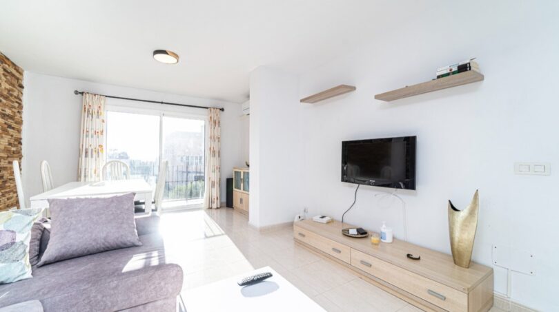 Helles Wohnzimmer in Artà mit grauem Sofa, Holz-TV-Möbel und Zugang zur sonnigen Terrasse.