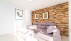 Wohnzimmer der Wohnung in Artà mit grauem Ecksofa, Holzsteinwand und modernen Kunstwerken
