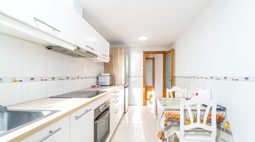 Moderne weiße Küche mit Esstisch, Einbaugeräten und Dekorfliesen in einer Wohnung in Artà.