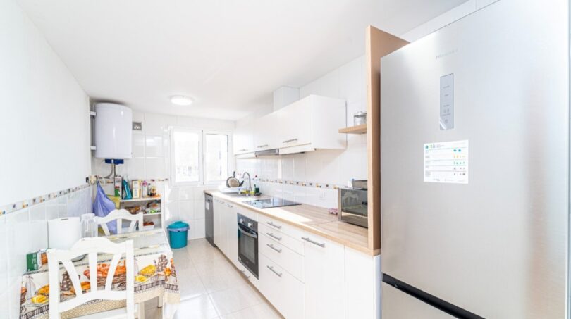 Helle Küche mit weißen Schränken, Holzarbeitsplatte, Einbaugeräten und Essbereich in Wohnung in Artà.