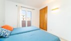 Bright bedroom of the apartment in Artà with blue beds, wooden wardrobe and balcony access.