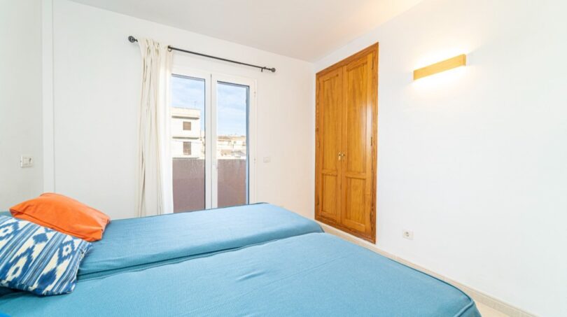 Bright bedroom of the apartment in Artà with blue beds, wooden wardrobe and balcony access.