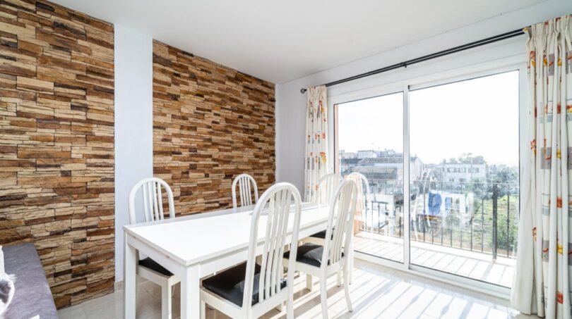 Helles Esszimmer mit weißem Tisch, Steinwandverkleidung und Balkon mit Stadtblick in Artà.