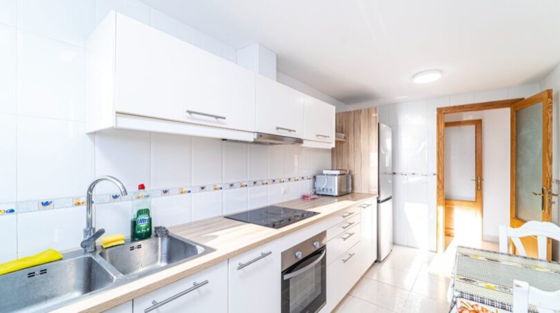 Moderne weiße Küche mit Einbaugeräten, Holzarbeitsplatte und Esstisch in Wohnung in Artà.