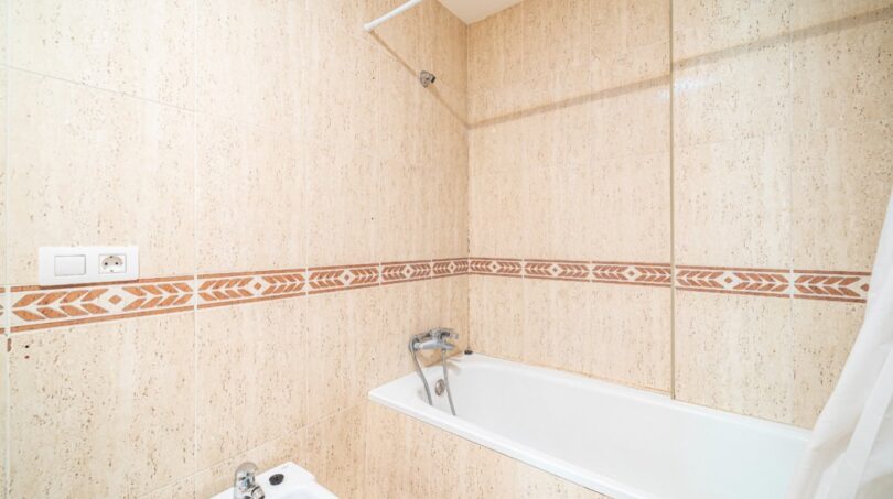Badezimmer mit Badewanne, Dusche und Bidet, beige Fliesenwände mit dekorativem Bordürenmuster in Artà