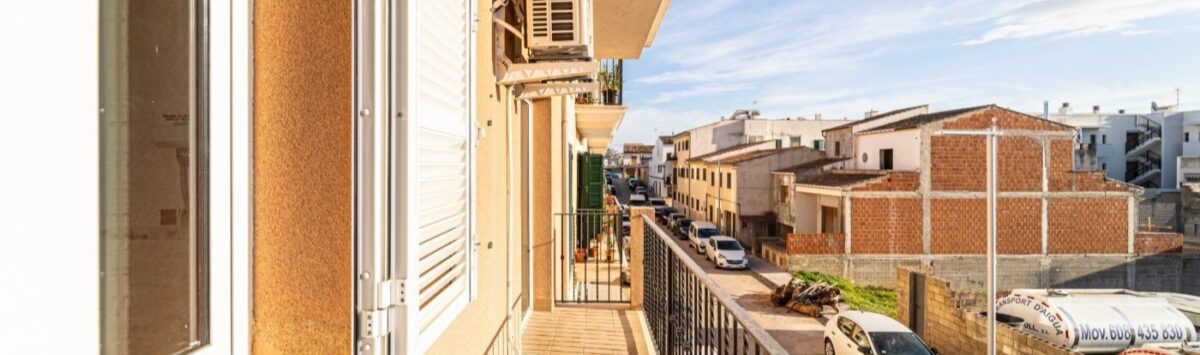 Sunny balcony of the apartment in Artà with metal railing, air conditioning and view of the quiet city street.