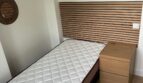 Kleines Schlafzimmer mit Einzelbett, Holz-Lattenoptik-Kopfteil, Nachttisch und Rattanspiegeln an weißer Wand.