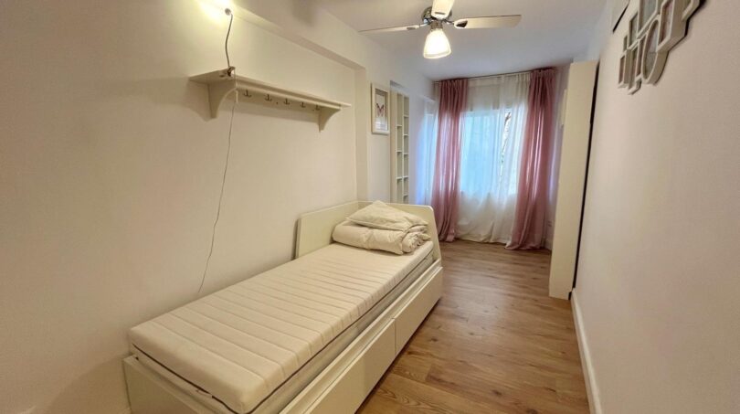 Helles Schlafzimmer mit Einzelbett, Holzboden, Deckenventilator und rosa Vorhängen in Strandnähe, Palma
